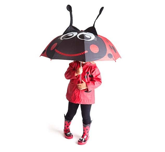 Child holding a ladybug-shaped umbrella with a red raincoat and matching boots on a white background