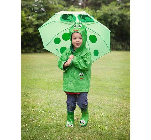 Child wearing a green raincoat, boots, and holding a matching umbrella outdoors.