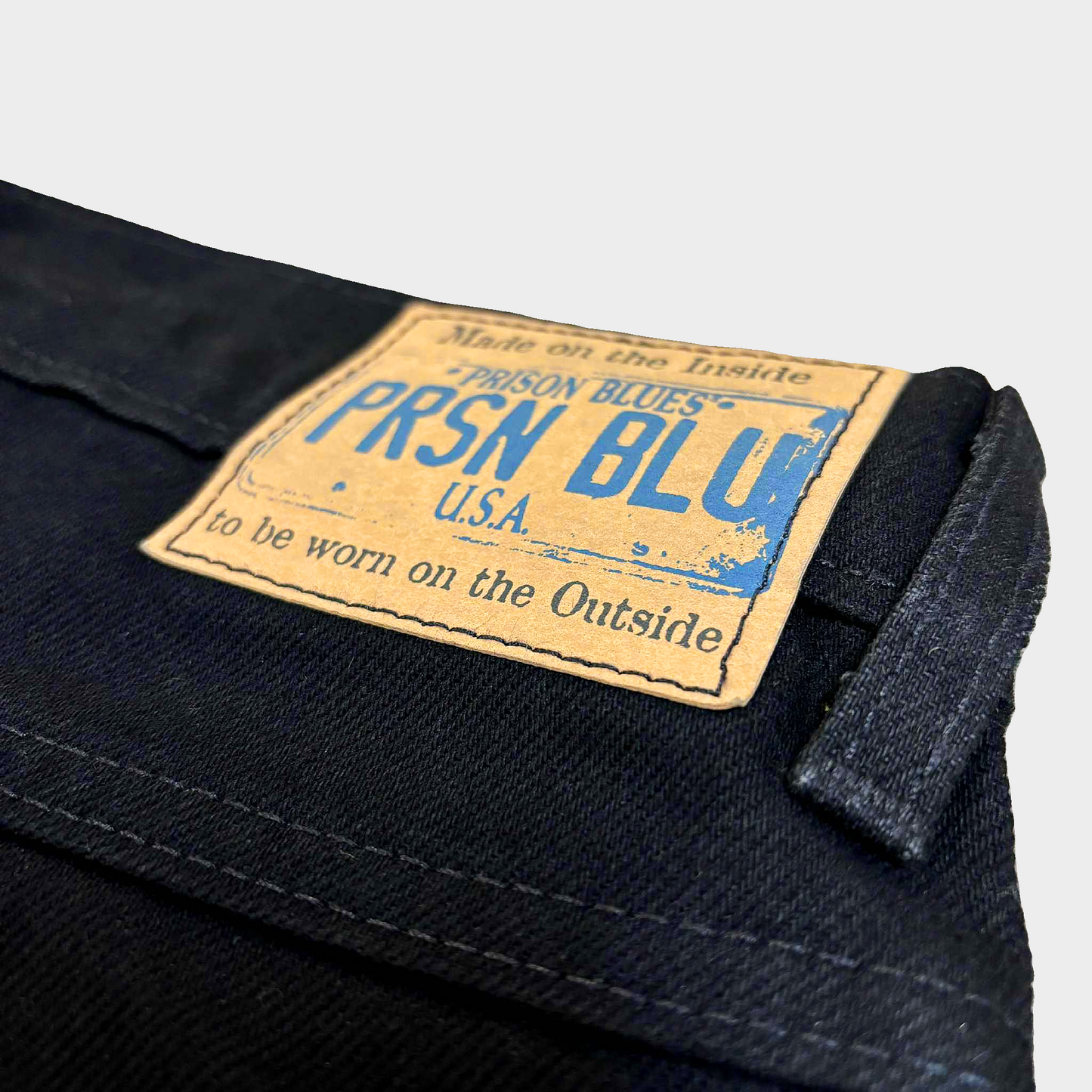 Close-up of a 'Prison Blues' label on dark denim fabric.