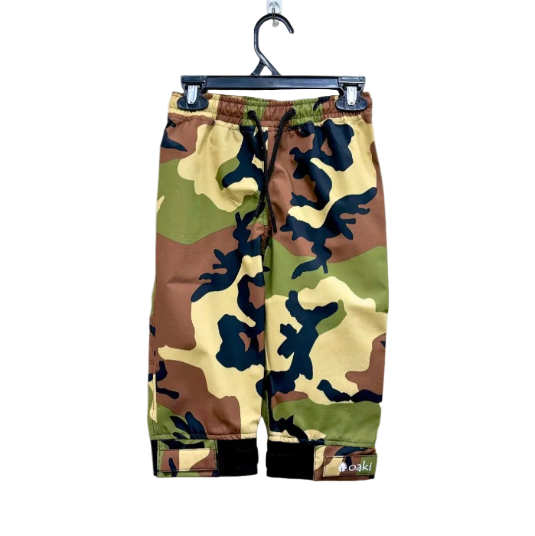 A pair of kids rain pants with an elastic waistband and drawstring. Ankles have a neoprene covered velcro adjustment. Shown in a classic camo pattern of green, brown, tan, and black